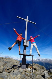 Hikers on the summit cross on the summit of Boeses Weibele Mountain in the Defregger Group