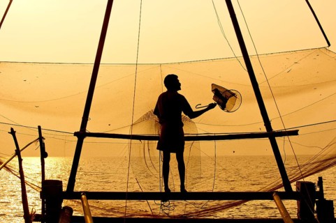 Fisherman holding a landing net in front of a Chinese fishing net at sunrise