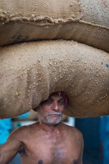 Elderly man carrying two bags filled with spices on his head