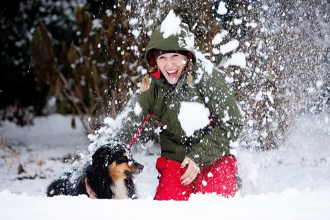 Young woman playing with an Australian Shepherd dog in the snow