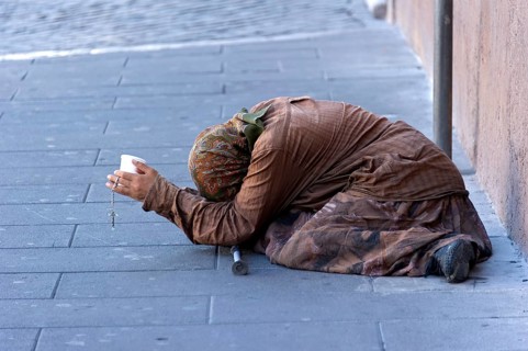Female beggar holding a plastic cup in a street of the old town