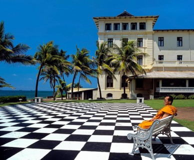 Monk sitting on a bench on a mosaic terrace in the garden in front of the Galle Face Hotel