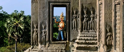 Temple dancer or apsara in a window of the temple of Angkor Wat beside apsara reliefs