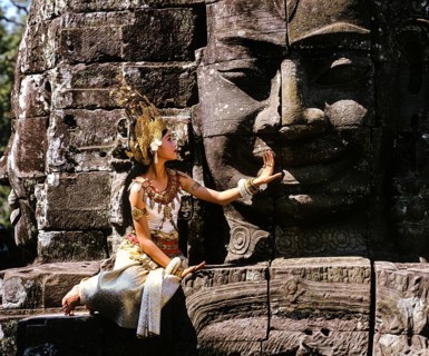 Temple dancer or apsara sitting in front of a face tower at Bayon Temple