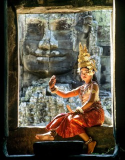Temple dancer or apsara sitting in a window in front of a face tower at Bayon Temple