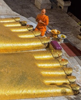 Monk praying at the feet of the golden Buddha statue of Wat Intharawihan