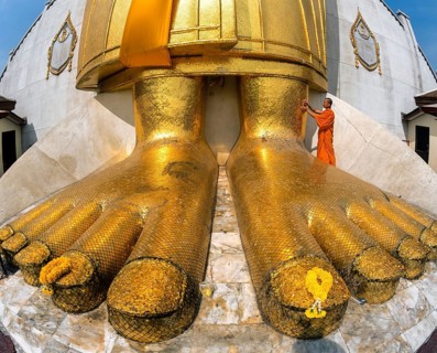 Monk praying at the feet of the golden Buddha statue of Wat Intharawihan
