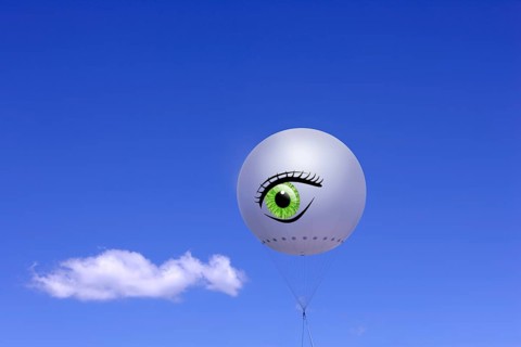 Tethered balloon with the illustration of a human eye against a blue sky with a cloud