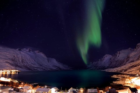 Aurora over a fjord with snow-covered mountains and an illuminated village