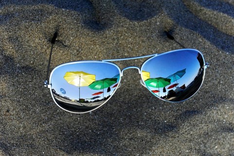 Parasols are reflected in sunglasses lying in the sand