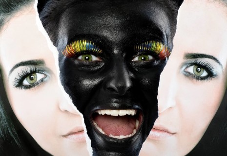 Face of a laughing young woman painted with black facepaint looking through a torn portrait photo