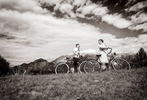 Man wearing leather pants and a woman wearing a dirndl with old bicycles within a natural landscape