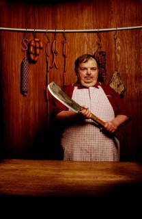 Fat butcher holding a meat cleaver in a butcher's store with a wooden ambience