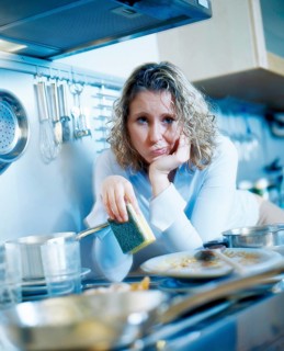 Annoyed woman holding a sponge while standing in a kitchen with dirty dishes