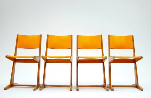 Four old orange school chairs standing side by side