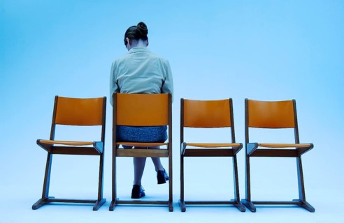 Woman wearing conservative clothes sitting on one of four orange chairs