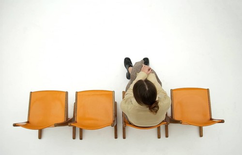 Woman wearing conservative clothes sitting on one of a row of four orange chairs