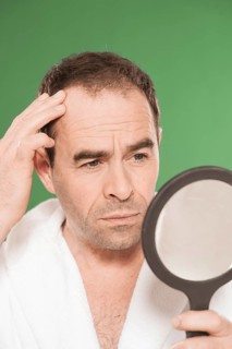 Man wearing a bathrobe observing himself critically in a hand mirror