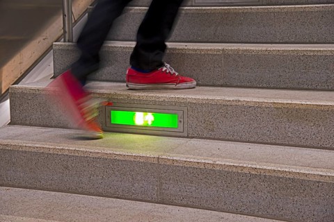 Person rushing up a public staircase with a green illuminated emergency exit sign