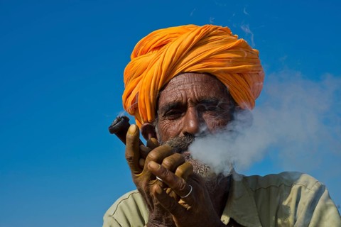 Elderly Rajasthani man with an orange turban smoking a hash pipe or hooka