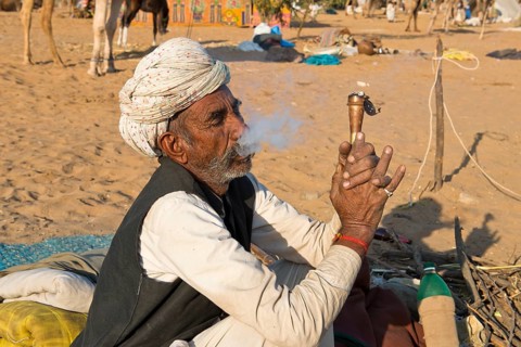 Indian with a turban sitting on the ground smoking a hash pipe