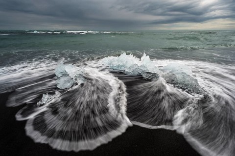 Pieces of ice on the black beach lapped by the sea