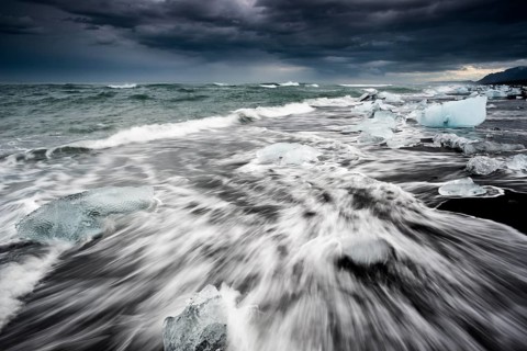Pieces of ice on black beach lapped by the sea