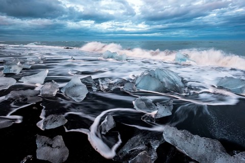 Pieces of ice on black beach lapped by the sea