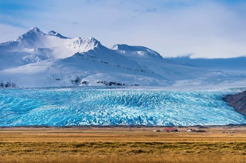 Icelandic farmstead with glacier tongue and snow-covered mountains
