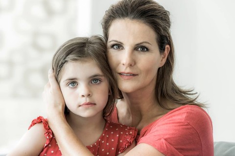 Mother and daughter sit together on the couch and look into the camera
