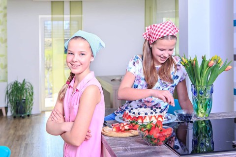 Teenage girls baking a cake at home with fresh fruit