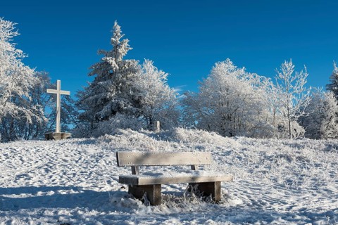 Snow-covered bench and summit cross on the Gaisberg