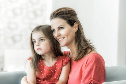 Mother and daughter sit together on the couch and look into the distance