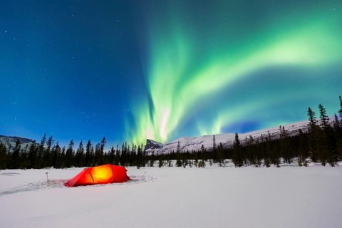 Northern Lights (Aurora borealis) above a red illuminated tent in winter