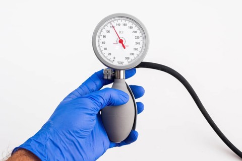 A hand with a blue medical glove is holding a sphygmomanometer