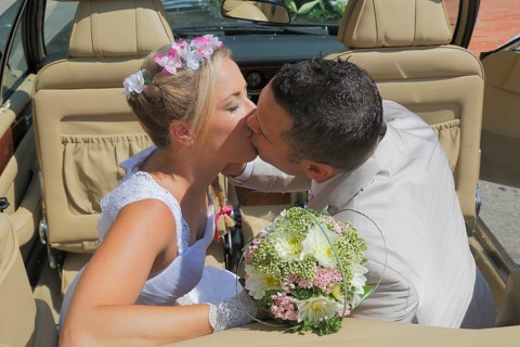 Bride and groom kissing in the back seat of an open car