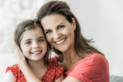 Mother and daughter sit together on the couch and look into the camera