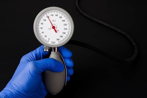 A hand with a blue medical glove is holding a sphygmomanometer