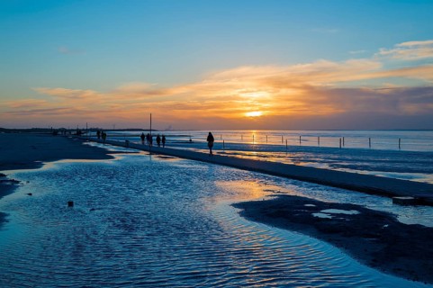 Beach walkers at the Wadden Sea on the North Sea coast in the blue hour at sunset
