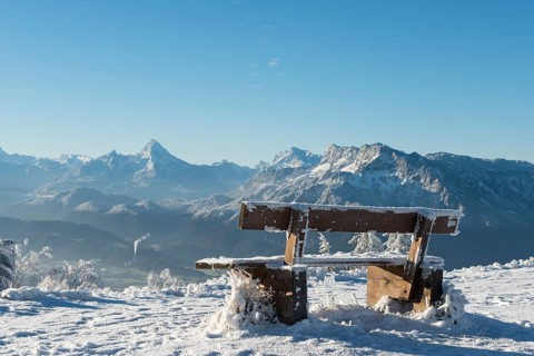 Snow-covered bench in front of Alpine panorama