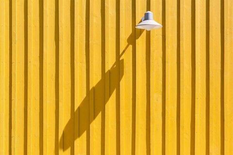 Lamp on a yellow beach hut casting a long shadow