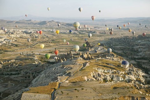 Hot air balloons rising over the cave dwellings and tufa formations in the morning light