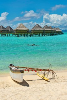 Decorated outrigger boat in front of overwater bungalows
