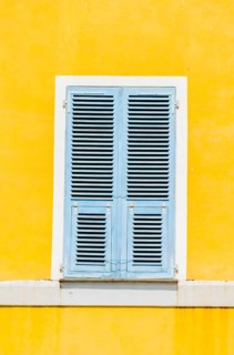 Yellow plastered wall with closed bright blue wooden shutters