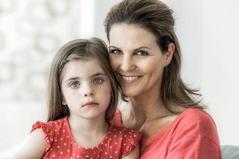 Mother and daughter sit together on the couch and look into the camera