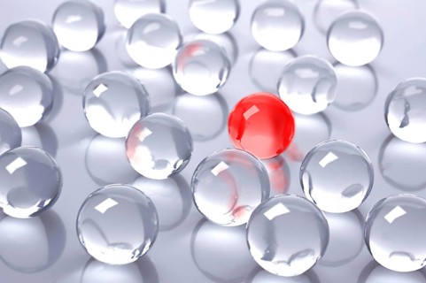 A red glass ball amidst many colourless glass balls
