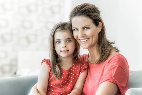 Mother and daughter sit together on the couch and look into the camera