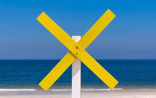 A yellow wooden cross marks a shoal near the shore at the beach