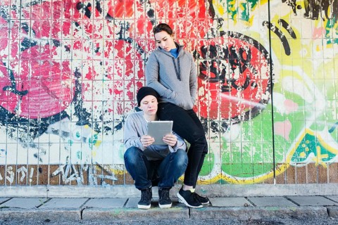 Casual and relaxed young man and woman reading on a notepad in front of grafitti wall in urban area
