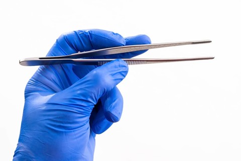 A hand with a blue medical glove is holding tweezers